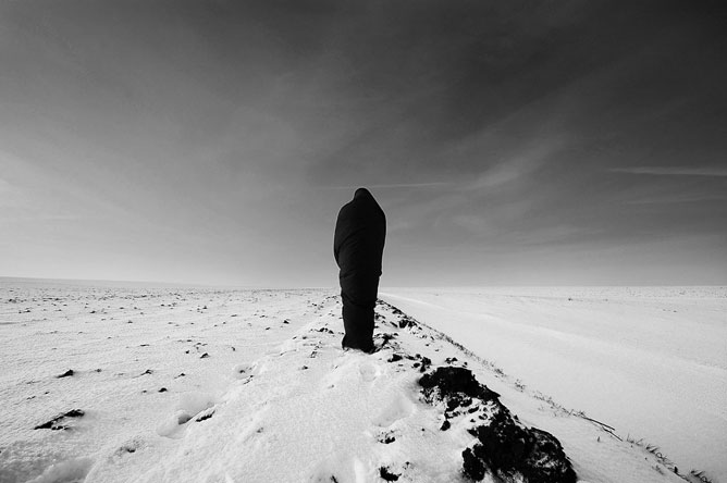 Fekete-fehér fotó egy alakról, aki háttal áll magában egy havas tájon