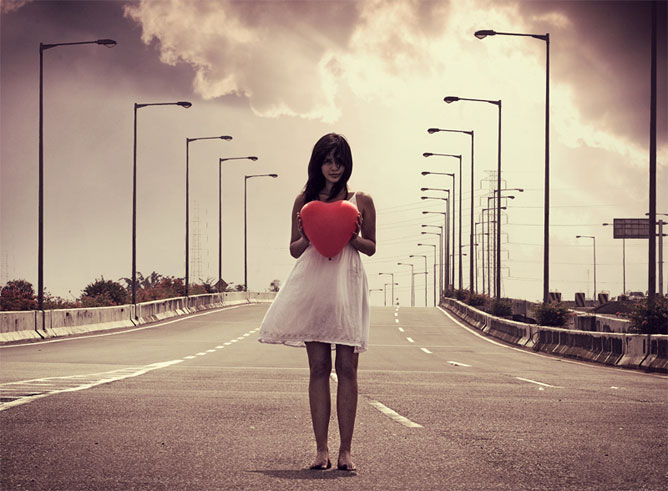 Egy út közepén álló fiatal lány piros szívvel a kezében.