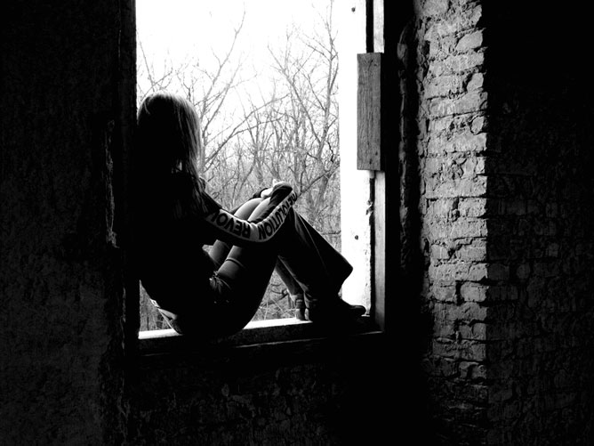 Szomorú lány egy romos épület ablakában.